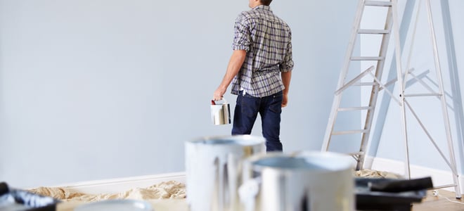 A man looks at a wall he is painting.