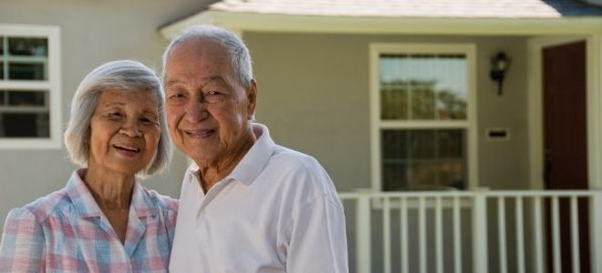 An elderly couple standing outside a house.