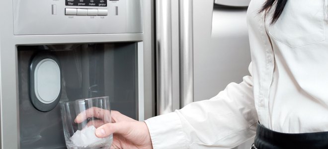 A woman getting ice in a glass from a refrigerator.