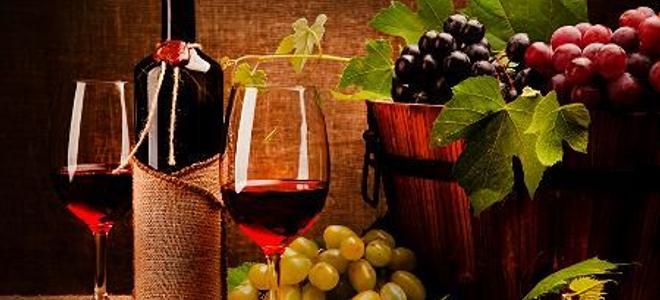 Full wine glasses and a bottle sitting next to a bucketful of grapes.