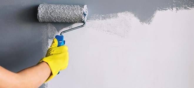A wall being painted gray with a paint roller. 