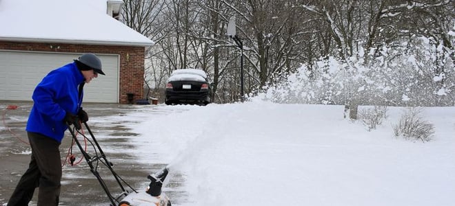 A man pushing a snow blower in a snow-covered yard. 