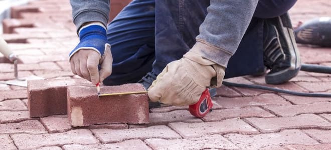 A close-up of a man measuring brick pavers. 