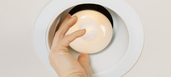 hand screwing a flood light into a recessed light fixture