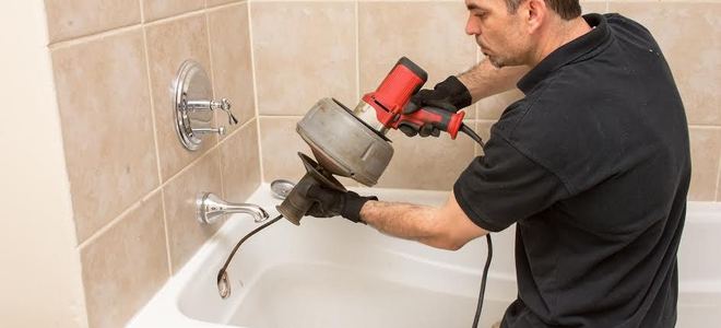 A plumber using a snake in a bathtub.