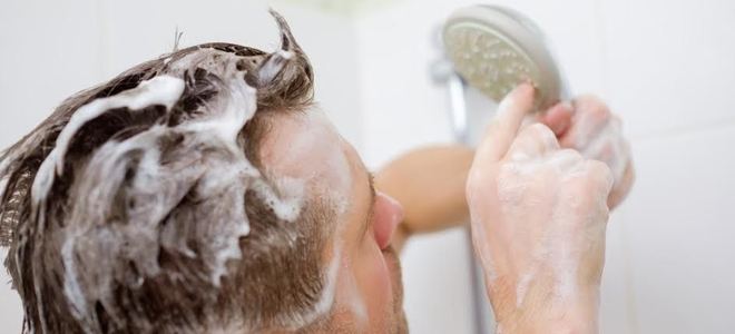 A man taking a shower and looking at the shower head in confusion.