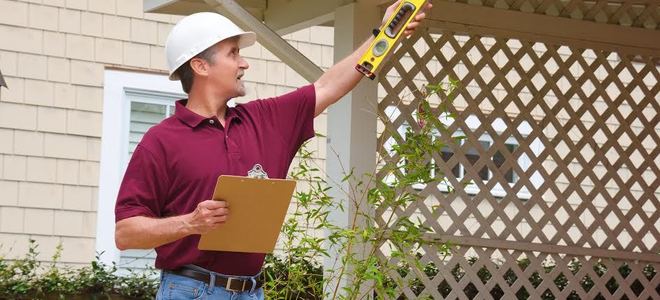 An inspector holding a clipboard and level while looking at a patio.
