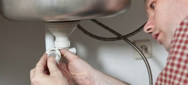A man installing kitchen sink plumbing.