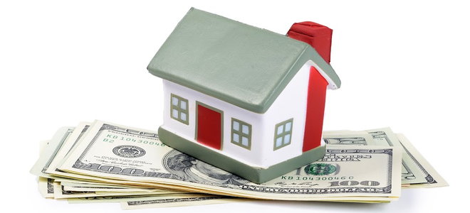 A small toy house on a stack of cash against a white background. 