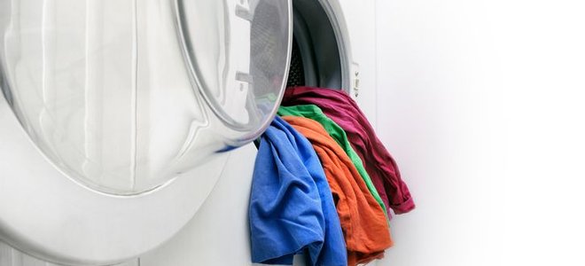 A rainbow selection of shirt hanging over the edge of a white washing machine basin.