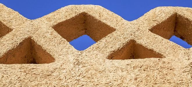 A fence against a blue sky made of rammed earth.