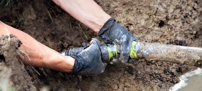 A drain pipe in mud with someone holding it.