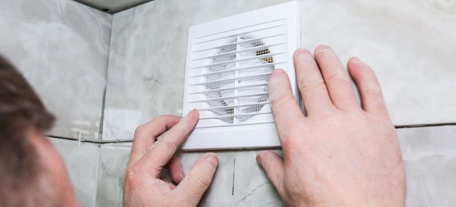 person adjusting a small exhaust fan on a tiled wall