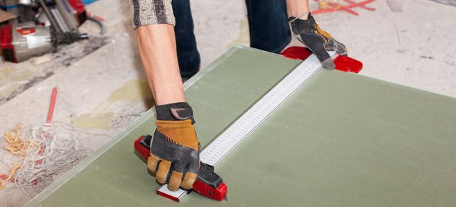 A person cutting greenboard with a utility knife. 
