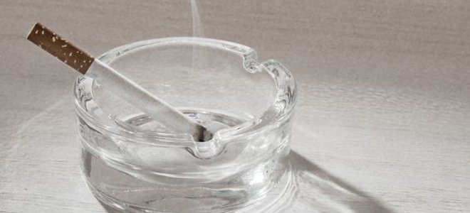 A smoking, lit cigarette in a clean glass ashtray.