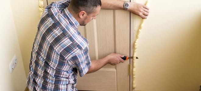 a man trimming foam insulation from a door jamb