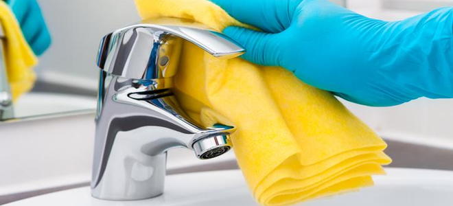 A chrome faucet being cleaned with a yellow cloth. 
