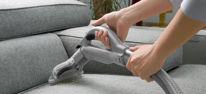Vacuuming a gray couch.
