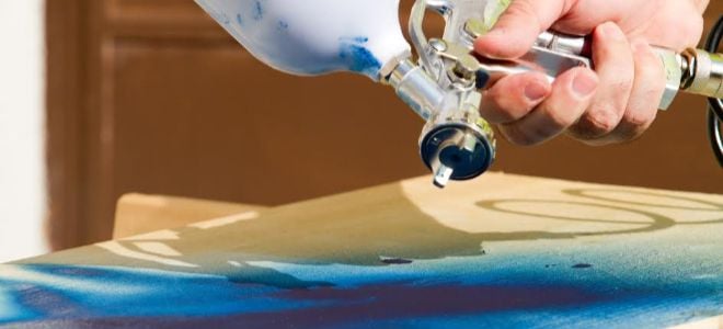 hand holding paint sprayer and applying blue paint