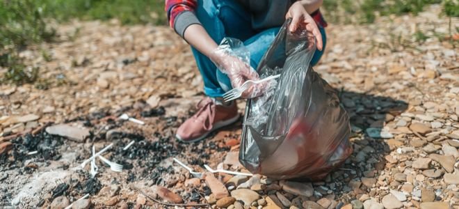 person filling a trash bag with trash from picnic site