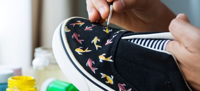 hand painting a fish pattern on black shoes