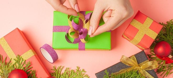 hands tying sparkly ribbon on a gift wrapped in green with holiday greens nearby