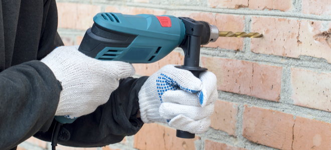 gloved hands drilling into brick wall