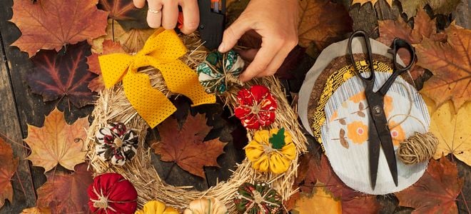 hands making autumnal wreath with glue, twigs, and fabric
