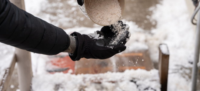 gloved hands applying salt to icy walkway