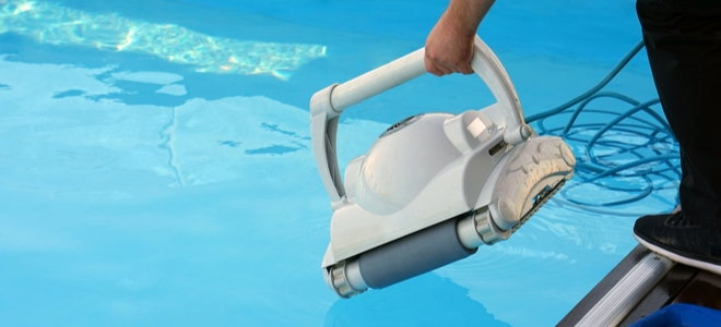 a hand lowers a pool cleaning robot into a pool