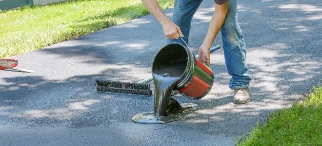 man pouring sealant on driveway