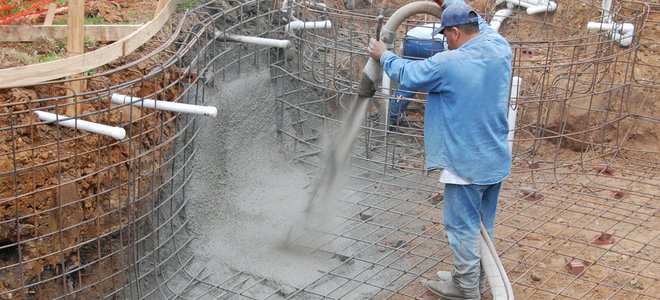 worker spraying shotcrete to form the base of a pool