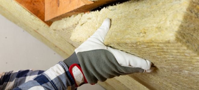 gloved hand adding insulation to panel in attic ceiling