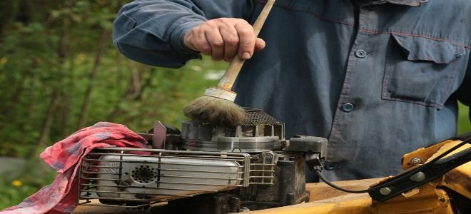 A man cleaning the engine of a lawn mower as part of a winterizing practice.
