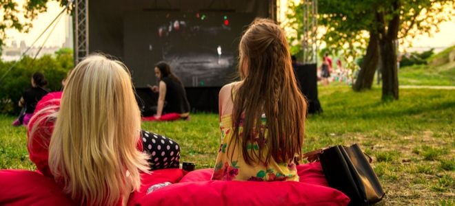 Girls lounge on pillows for an outdoor movie.