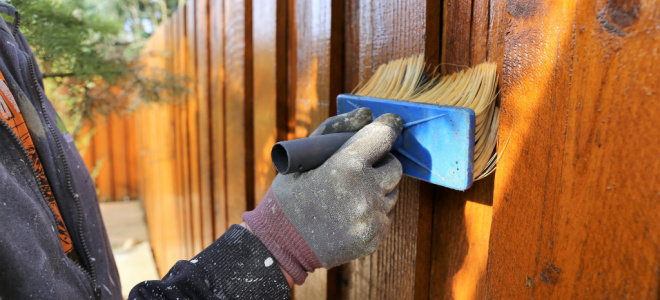 gloved hand staining fence with brush