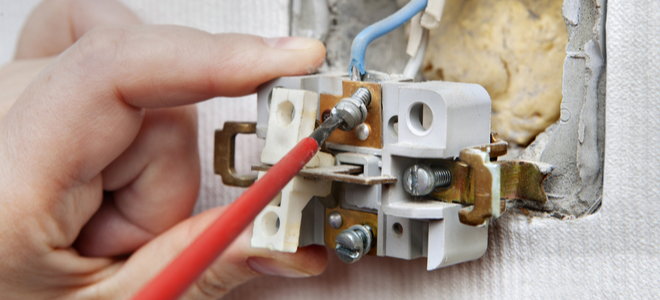 hand reattaching light switch wiring to wall
