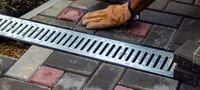 hand installing patio bricks around a drainage gutter