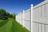 New and contemporary white vinyl fence running across a nicely landscaped backyard with lawn and blue sky.