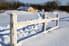 A snow fence surrounded by snow with a house in the background.