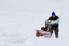 A man trudging through heavy snow, pushing a snowthrower.