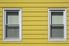 Yellow aluminum siding with two windows.