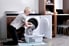 A woman on her knees putting laundry in a washing machine.