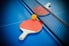 Two ping pong paddles and a ball laying on a blue table.