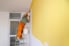 A painter covering a white wall in yellow interior paint.
