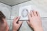 person adjusting a small exhaust fan on a tiled wall