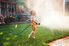 A girl holding a hose that's spraying water all over a lawn in a backyard.
