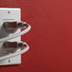 Two cords are plugged into an electrical outlet on a red wall.