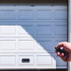 hand with clicker pointing at opening or closing roll up garage door