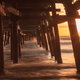 sun setting on an ocean under a wooden pier